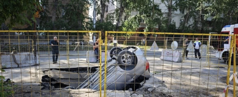 Легковой автомобиль лежит на крыше после падения в глубокий провал асфальта на перекрестке улиц Мичурина и Фрунзе в Новосибирске.