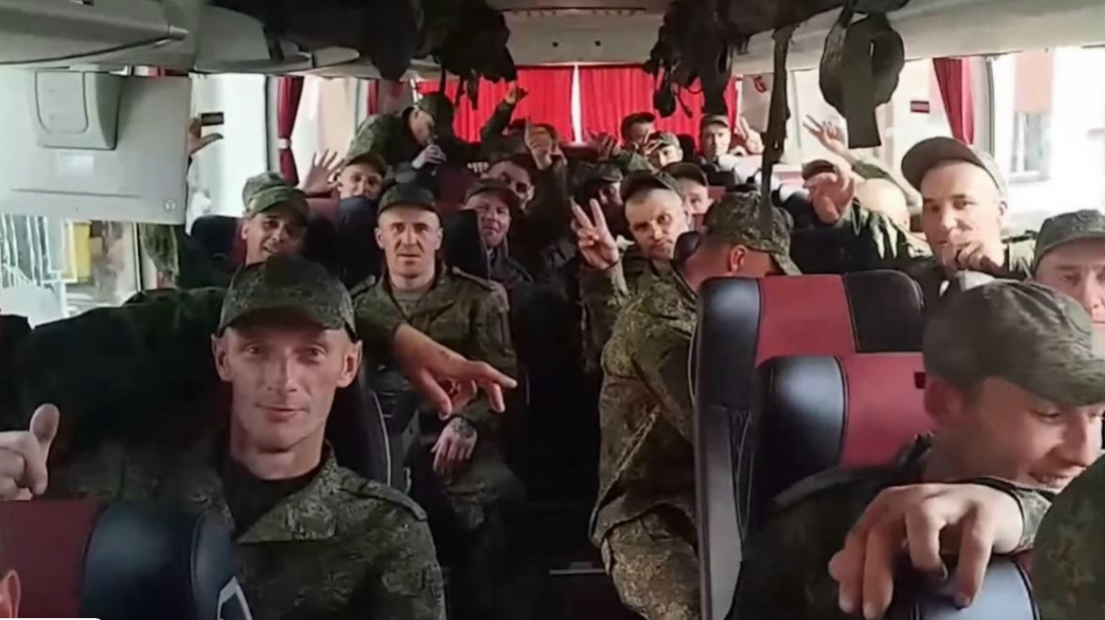 Группа российских военнослужащих в гражданской одежде выходит из автобуса на территории аэродрома после освобождения из плена