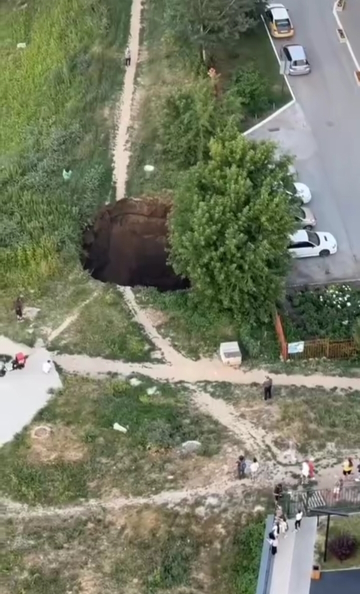Огромная глубокая яма, образовавшаяся на месте асфальтового покрытия во дворе жилого дома в Новосибирске.