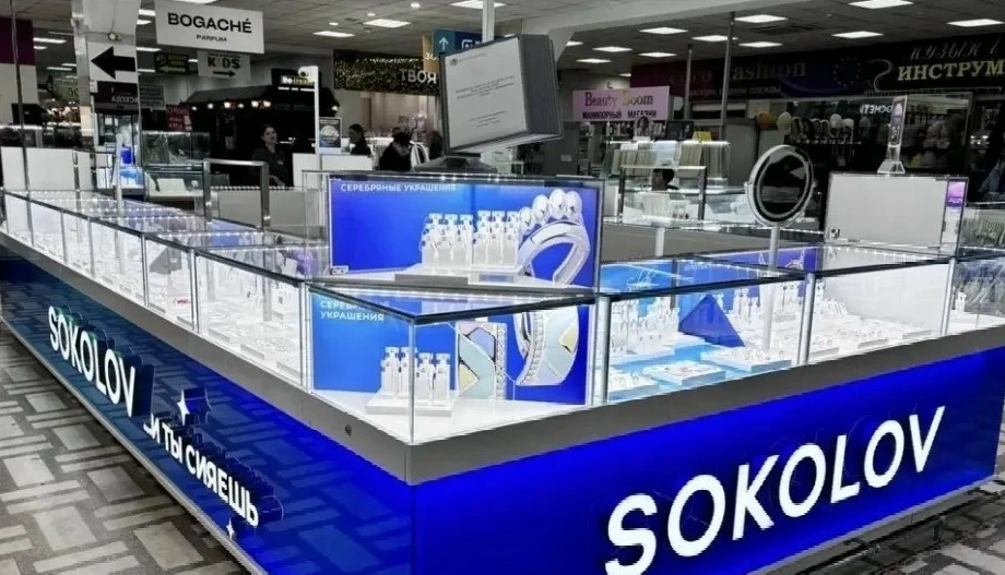 Витрина фирменного ювелирного магазина с золотыми украшениями и драгоценными камнями под стеклом.
